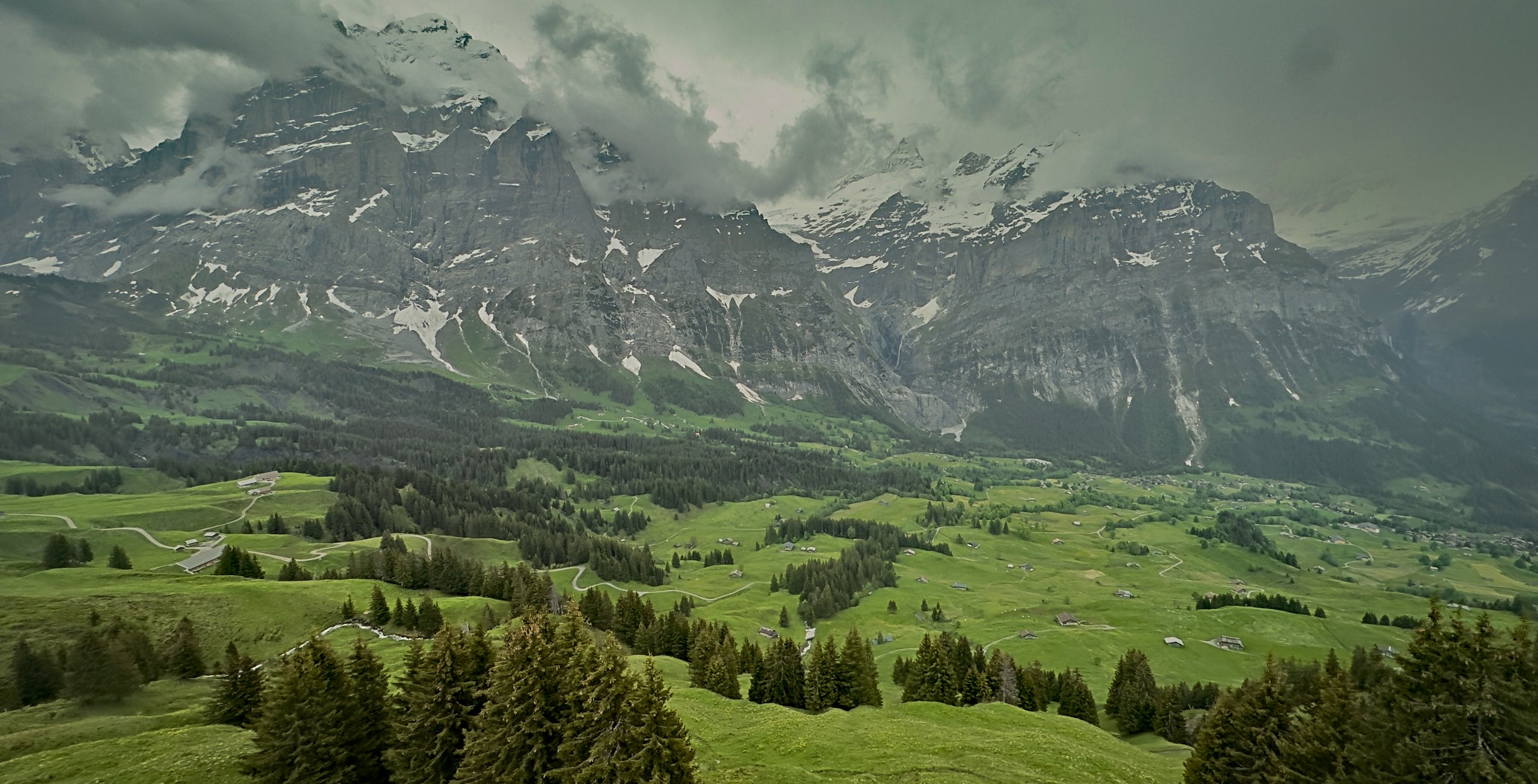 Cloud over snow-streaked mountains above a green Swiss alpine valley